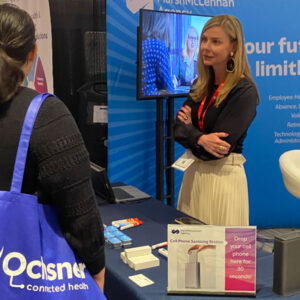 Conference participant engaging with a healthcare booth featuring a cell phone sanitizing station.