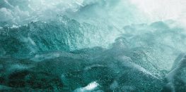 Aerial view of frothy ocean waves with a glass-like texture in shades of turquoise.